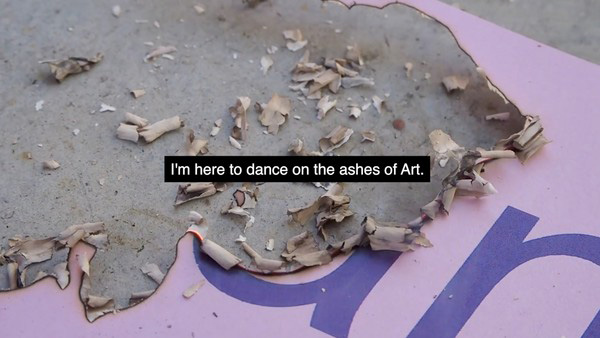 A pink flyer with illegible purple text lays on a concrete background. The flyer has been burned and its ashes are falling onto the concrete. In the middle of the image, small white letters over a black bar read, I'm here to dance on the ashes of Art.