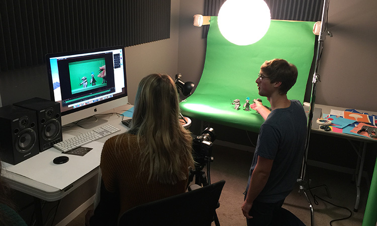 Students work with a computer and green screen to create stop-motion animation