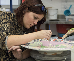 A student paint on a ceramic piece