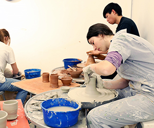 A student working on a throwing wheel with other students in the background