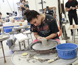 A student works with a piece on a throwing wheel