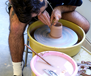 A student works with a vessel on a throwing wheel