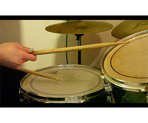 Video still of a drum kit and hands holding drumsticks