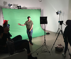 Students watch an instructor talk in front of a green screen in a studio